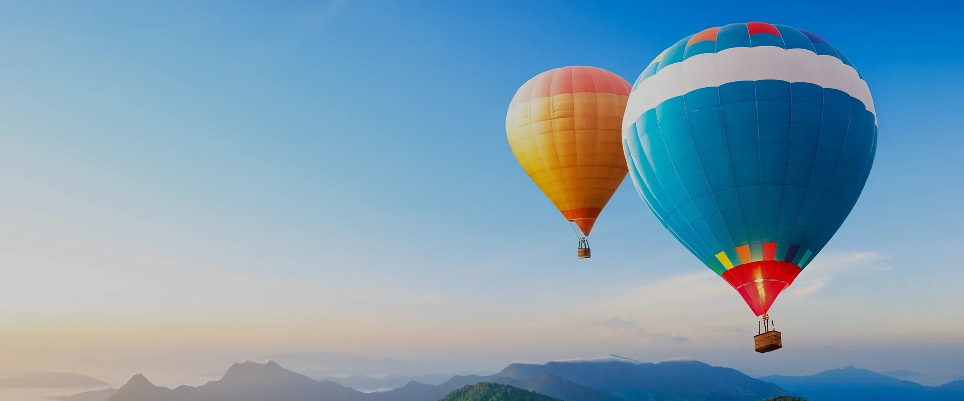 Two hot air balloons flying over a mountain range.